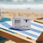 Beach Tallow Balm - 40ml by Bare Bones Beauty in a metal tin on a blue-striped chair at the beach.