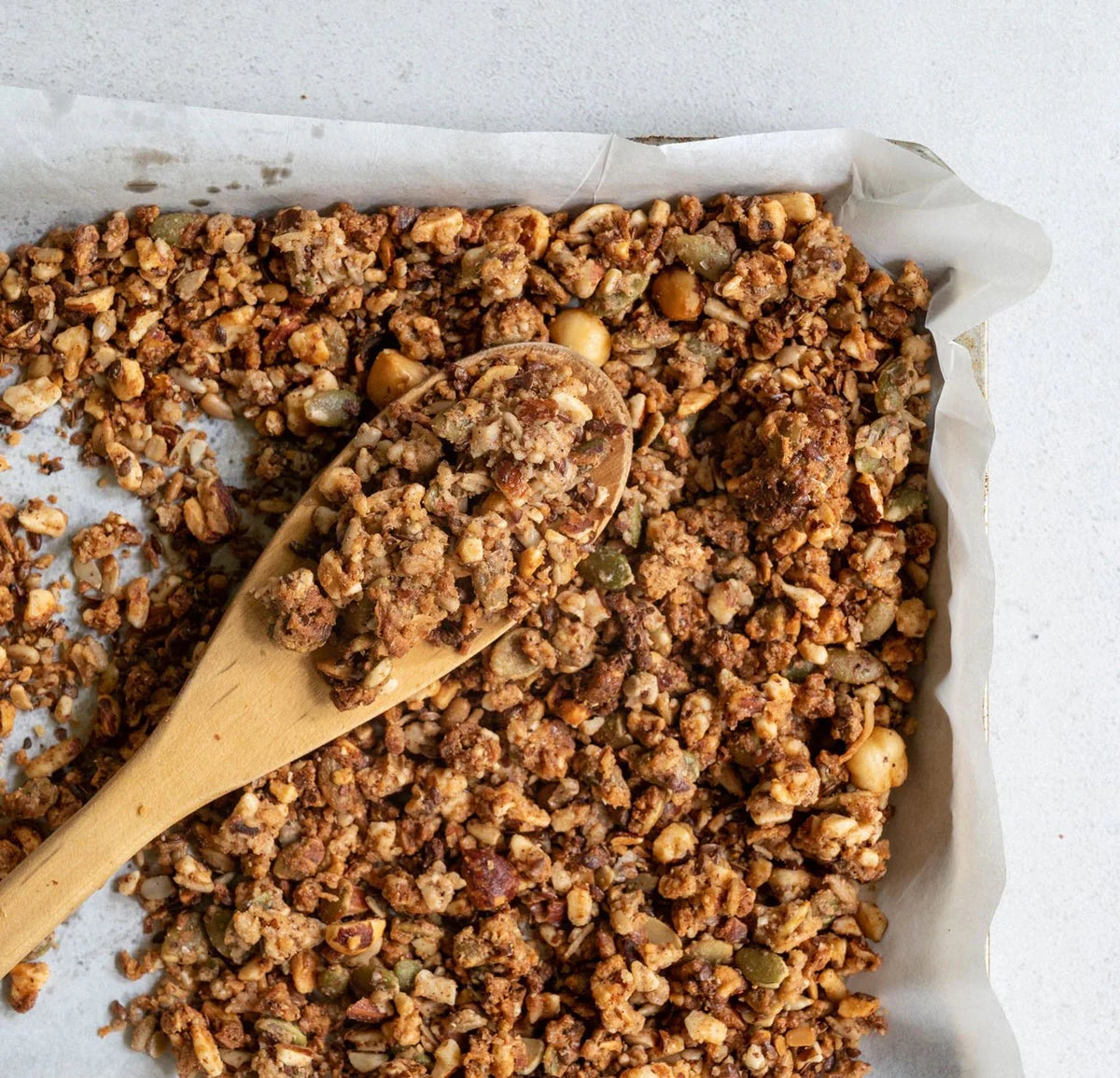 The Monday Food Co roasted hazelnut granola on a baking tray with a wooden spoon