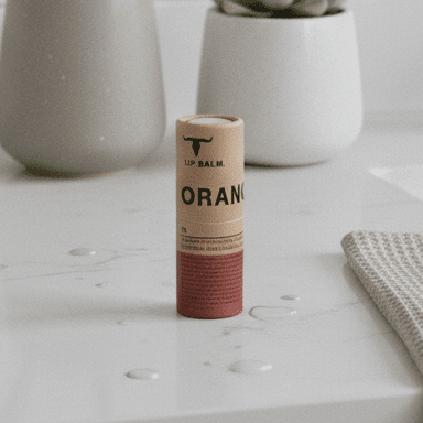 Orange Lip Balm - 7g by Bare Bones Beauty standing on a white surface with plants and a cloth in the background