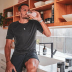 Man in black activewear drinking from branded shaker in kitchen with Triple Magnesium Powder - Lemon Lime - 200g jars nearby