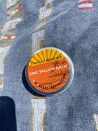Zinc Tallow Balm - 130g in small round tin with orange label by Barefoot Skincare Co on blue fabric background